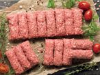 Сурови кюфтенца, нарязани на парчета, подредени на хартия за печене.