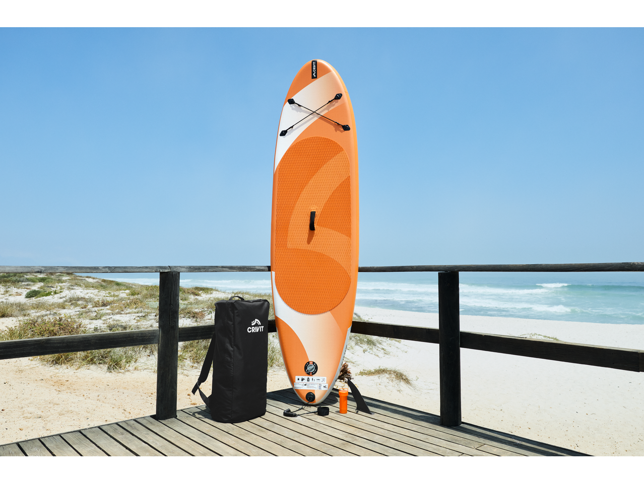 Prancha de SUP Crivit e mochila num terraço de madeira junto à praia.