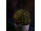 Solar-powered LED string lights on a potted topiary bush at night.