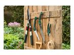 Gardening tools including hedge shears, folding saws, and pruning shears hanging on a wooden fence in a garden.
