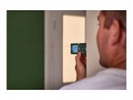 Man using a laser distance meter to measure a room, with a red laser line visible.
