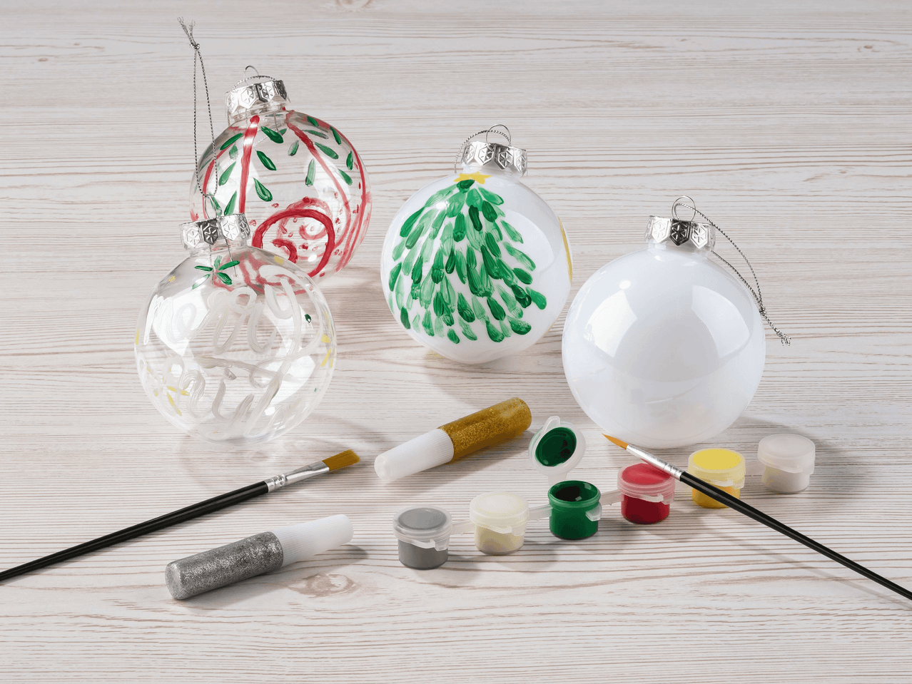 Weihnachtskugeln mit Farben und Pinseln zum Bemalen auf einem Holztisch