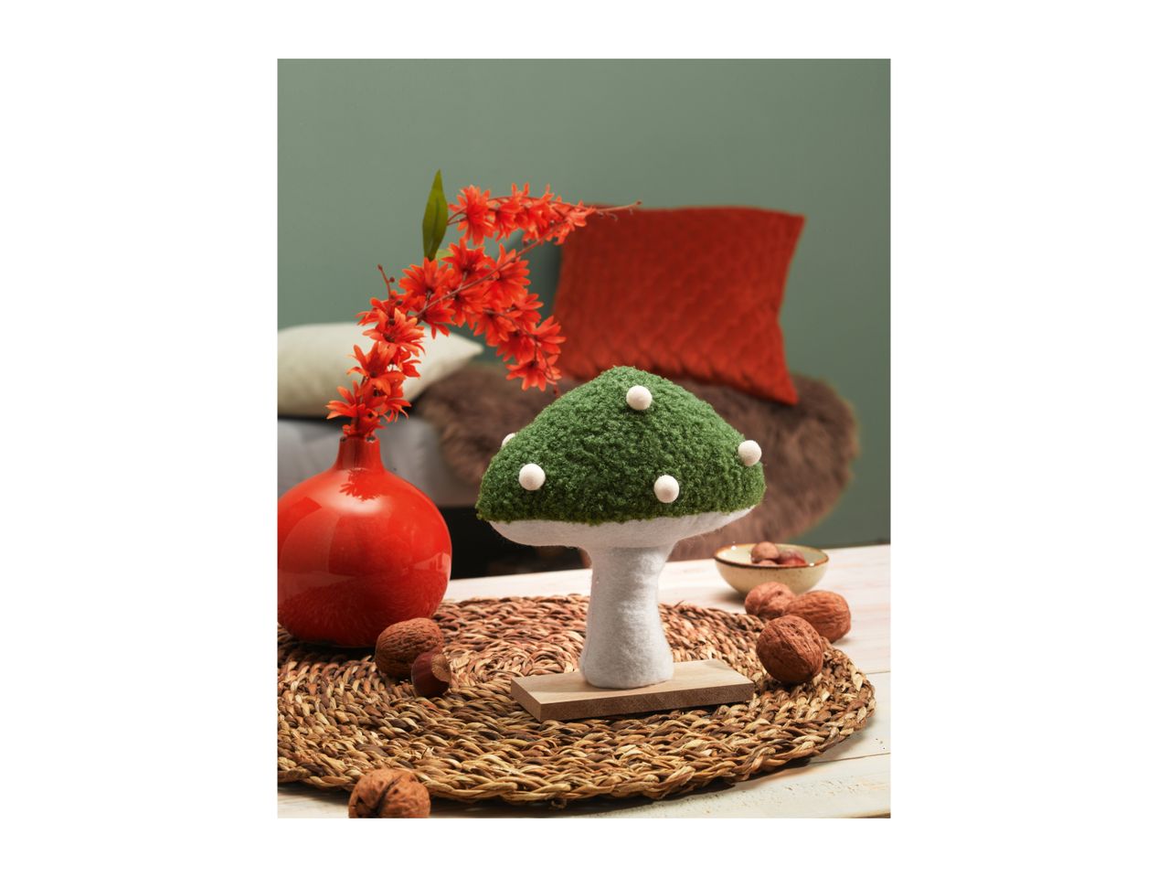 A decorative green mushroom with white spots, red flowers in a vase, and walnuts.