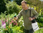 Man spraying plants in a garden with a garden sprayer.
