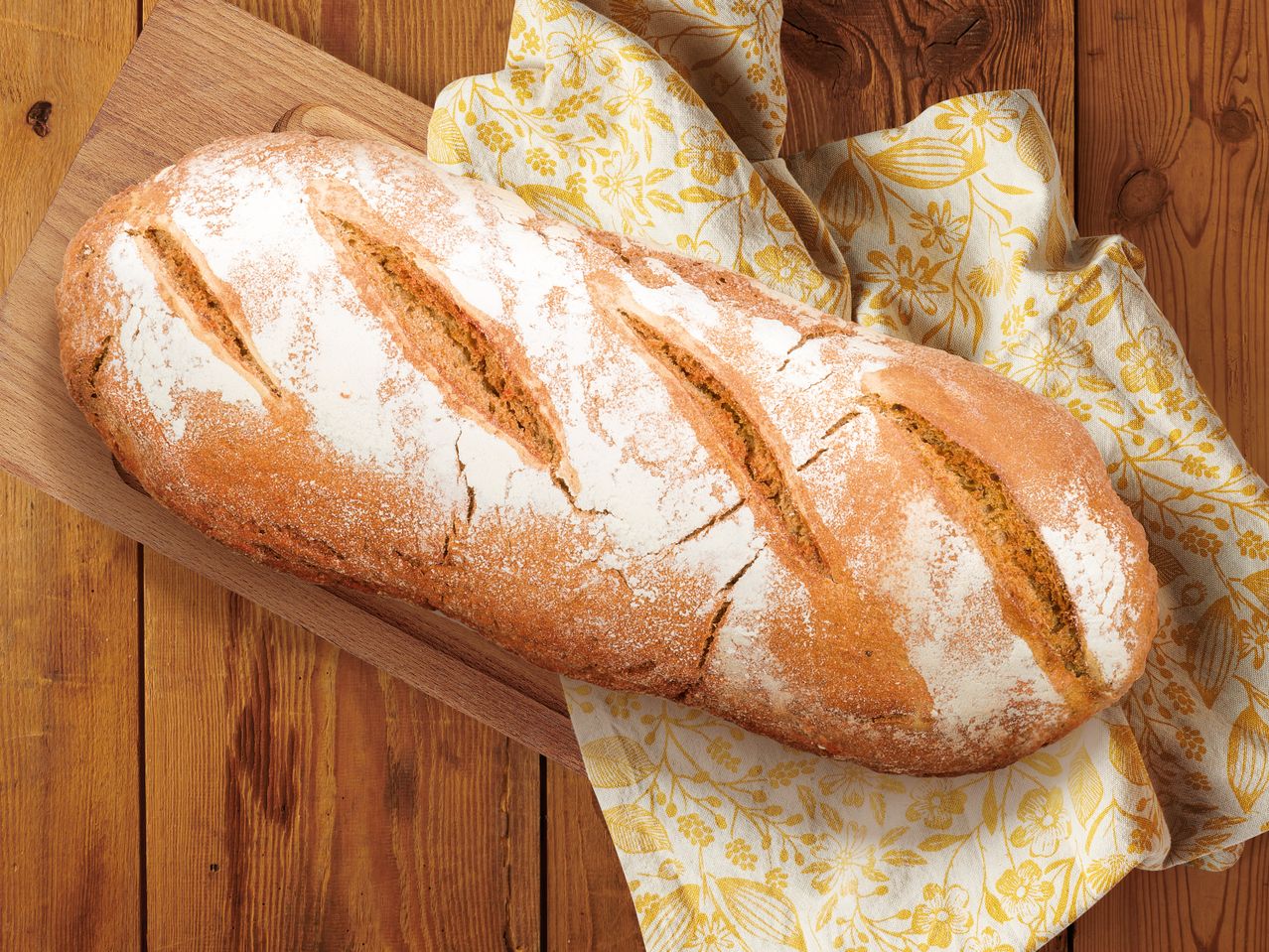 Прясно изпечен хляб на дървена дъска, с цветна кърпа.