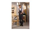 Man in work overalls holding a power tool in a workshop with tools on a wooden board.