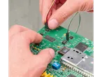 Mâini conectând fire la o placă de circuit verde cu microcipuri și componente.