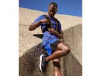 Man in blue athletic wear and hydration vest, taking an energy gel break during a run.