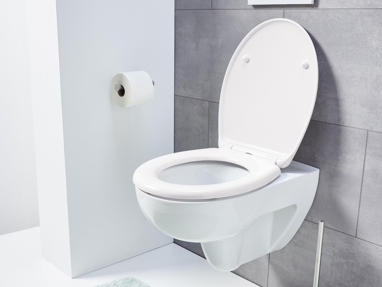 Fehér fali WC nyitott ülőkével és WC-papír tartóval egy modern fürdőszobában.