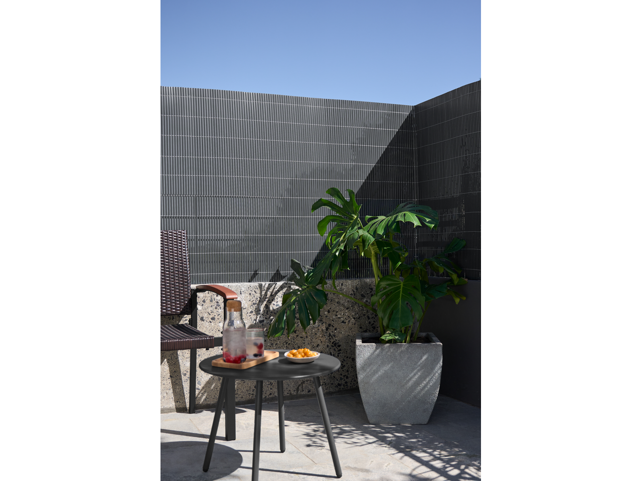 Outdoor patio with a small table, drinks, snacks, a chair, and a large potted plant.