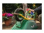 A person spraying lubricant on a wheelbarrow wheel, with potted flowers in the background.