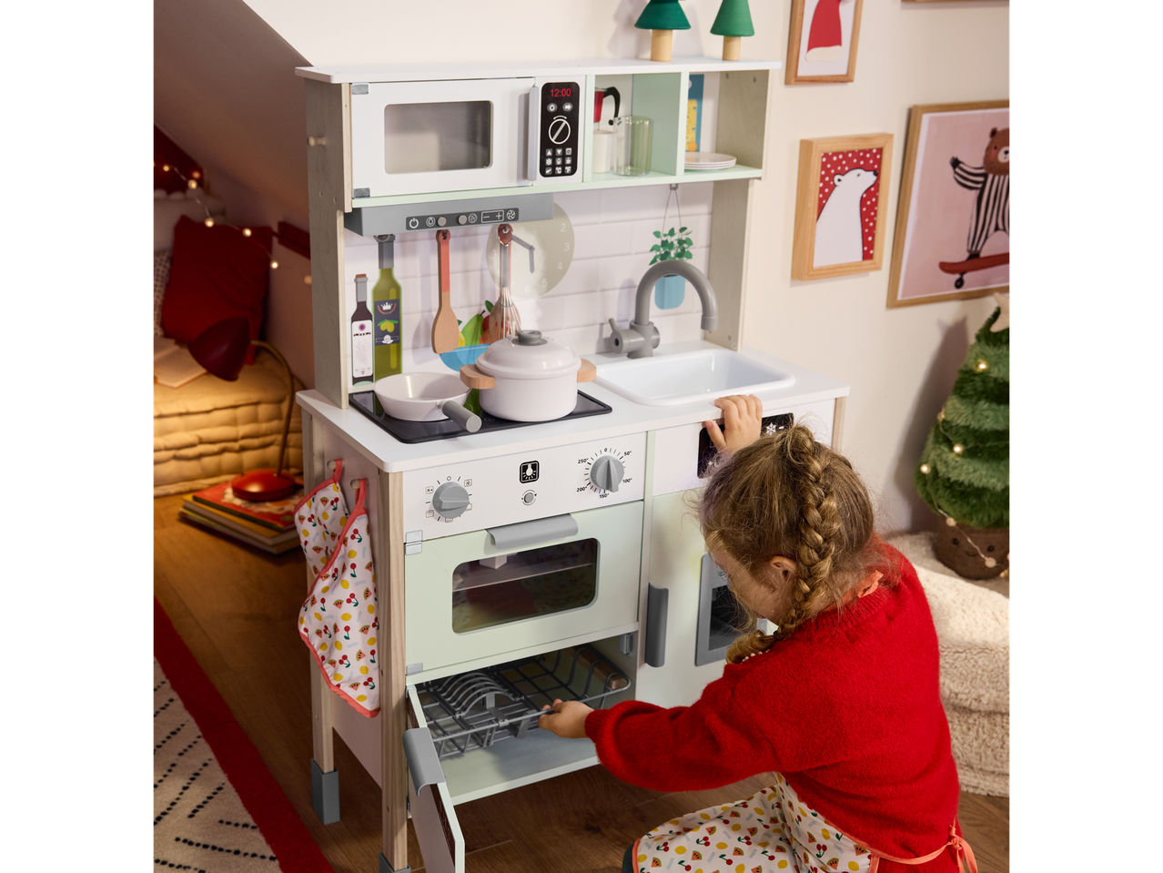 Girl playing with a white wooden play kitchen featuring an oven and microwave.