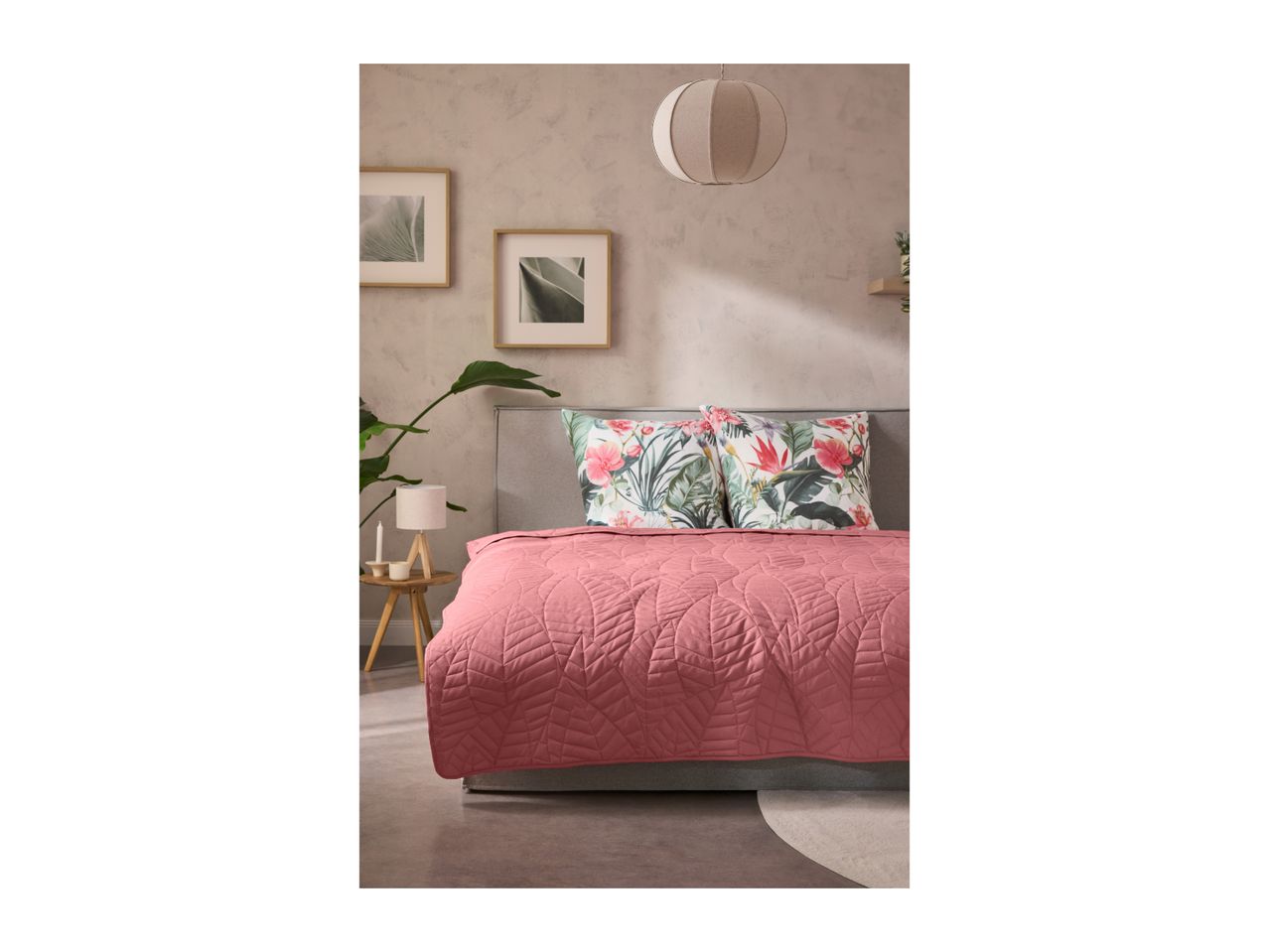 Bedroom with a pink quilted bedspread, floral pillows, and framed botanical prints.