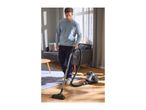 A man vacuuming a wooden floor with a canister vacuum cleaner in a living room.
