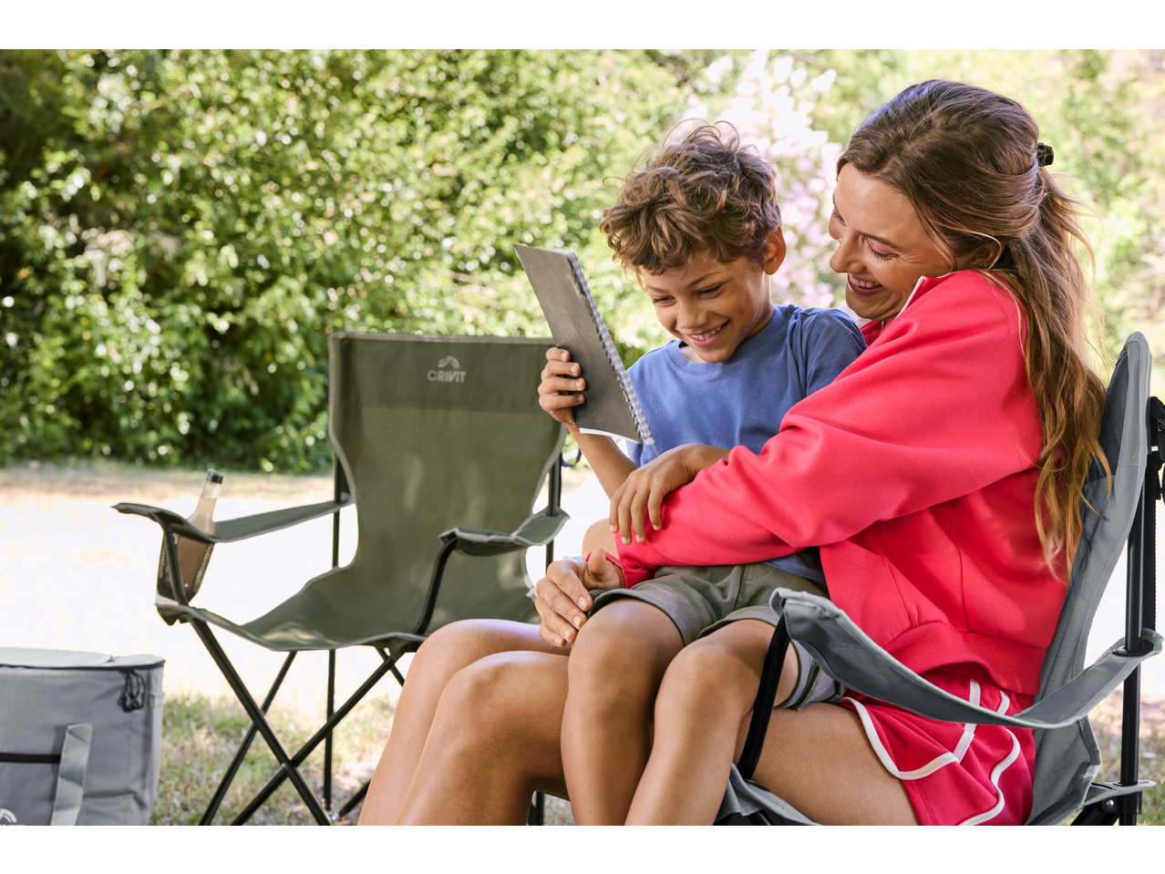 Happy mother and child on CRIVIT Folding Camping Chairs, looking at a notebook.