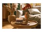 A lit candle and a vase with orange flowers on a wooden side table in a cozy living room.