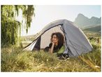 Une femme se repose dans une tente de camping Quechua, près d'un lac et de montagnes.