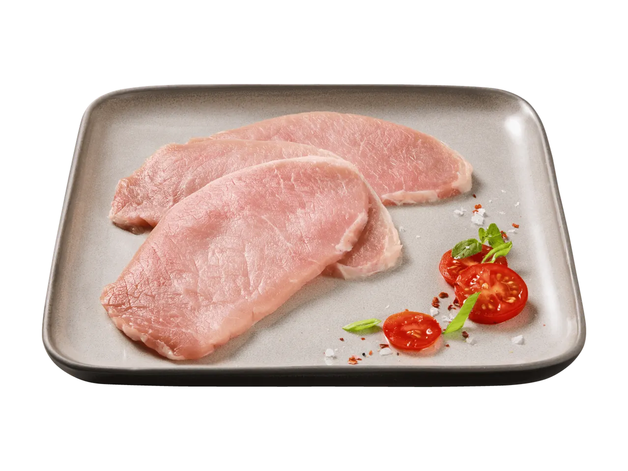 Rohe Schweineschnitzel auf einem Teller mit Tomaten und Kräutern.