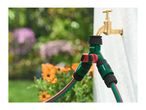 Garden tap with a two-way hose splitter and two green garden hoses, surrounded by flowers.