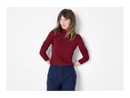 Woman in a red ribbed turtleneck and navy blue trousers, hands on hips, looking left.