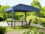 A navy blue pop-up gazebo provides shade over a patio table and chairs in a lush garden setting.