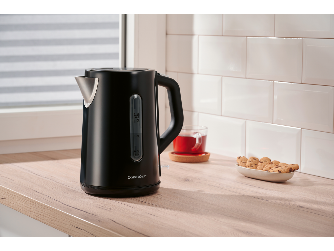 Black electric kettle on a wooden countertop with tea and cookies.