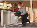 A woman uses a Parkside paint sprayer to paint a radiator in a workshop.