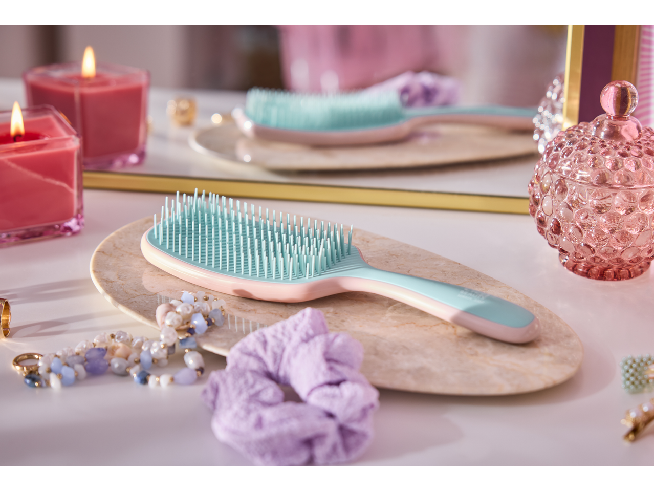 Escova de cabelo CIEN BEAUTY rosa e turquesa numa penteadeira com velas e acessórios.
