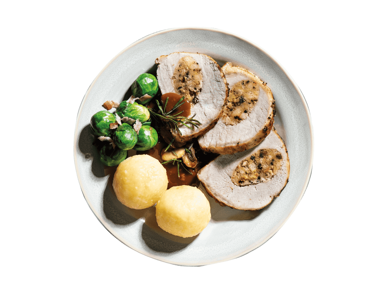Gefüllter Schweinebraten mit Rosenkohl, Knödeln und Soße auf einem Teller.