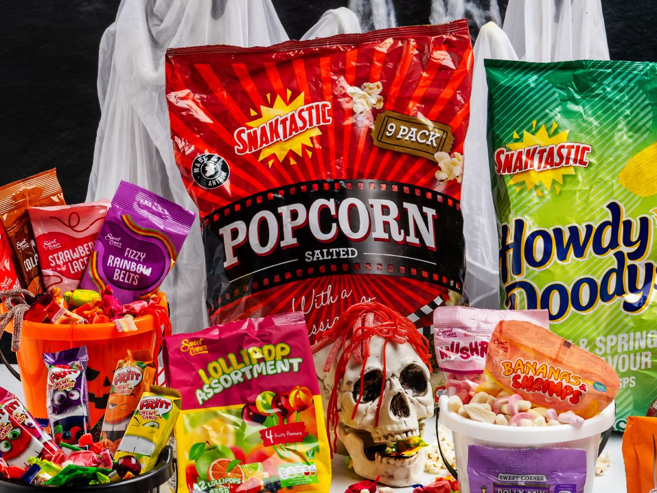Halloween-themed snack display with popcorn, chips, and various candies, including a skull decoration.