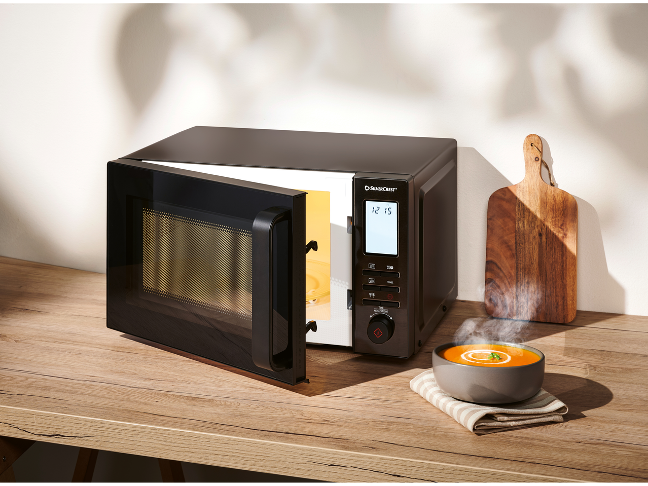 Silvercrest microwave with an open door and a bowl of hot soup on a wooden countertop.