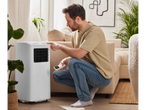 Man operating a portable air conditioner with remote in living room.