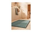 A teal bath mat on a light-colored tiled bathroom floor.