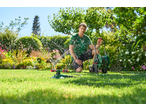 Man watering a lush green garden with a sprinkler and hose reel.
