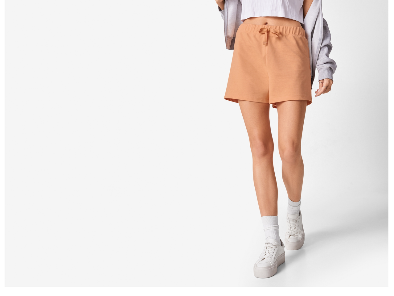 Femeie în pantaloni scurți de culoare piersică și adidași albi.