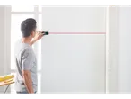 Bărbat folosind un telemetru laser pentru a proiecta o linie roșie pe un perete alb.