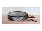Crepe maker on a wooden counter with a plate of crepes, strawberries, and ice cream.