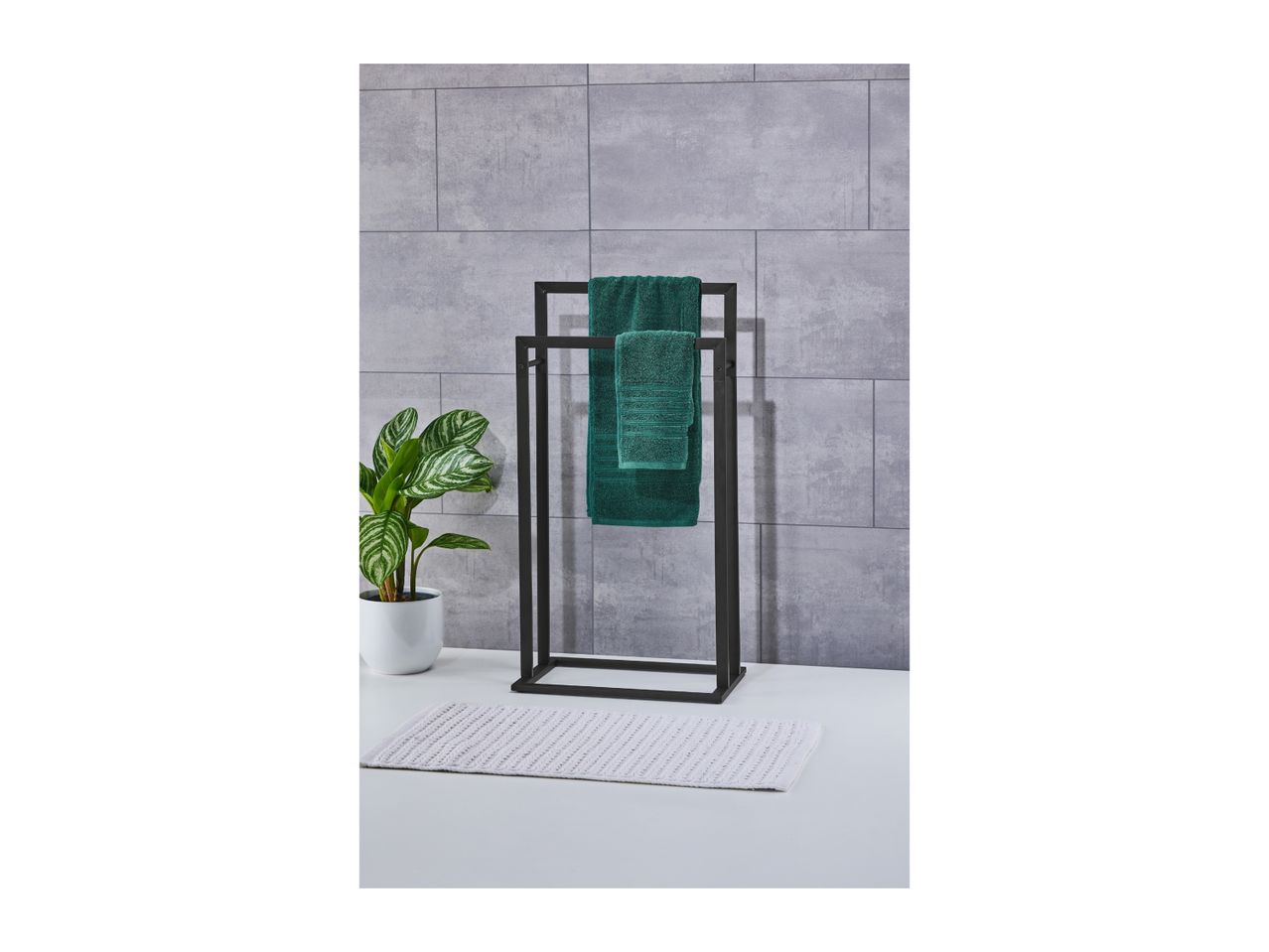 Black towel rack with green towels, a potted plant, and a white bath mat.