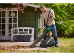 Man using a Parkside leaf blower to clear leaves from a patio next to a green shed.