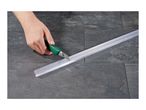 Hand cutting a clear plastic shower seal with a utility knife on a dark tiled floor.