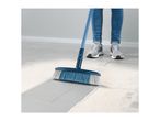 A person sweeps a floor with a long-handled brush.