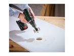 Cordless drill with a hole saw cutting into a white board, creating sawdust.