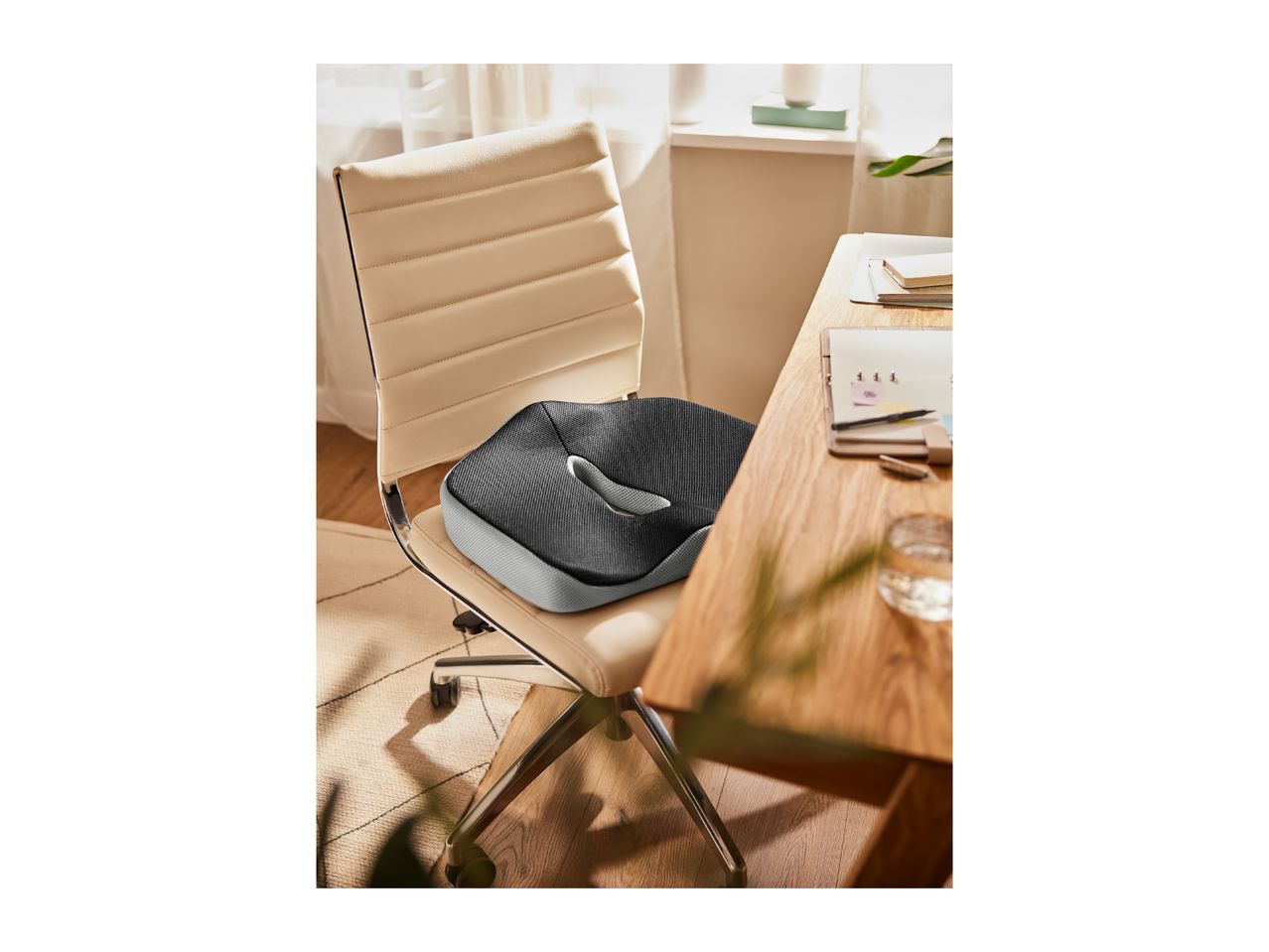 An ergonomic seat cushion on a beige office chair next to a wooden desk.