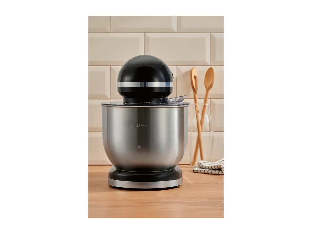 A black and silver stand mixer on a wooden countertop in front of a tiled wall.