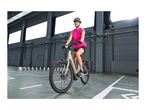 Woman in a pink vest and helmet riding a bicycle in a large indoor space.