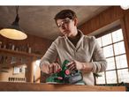 A person uses a Parkside Electric planer to smooth a piece of wood in a workshop.