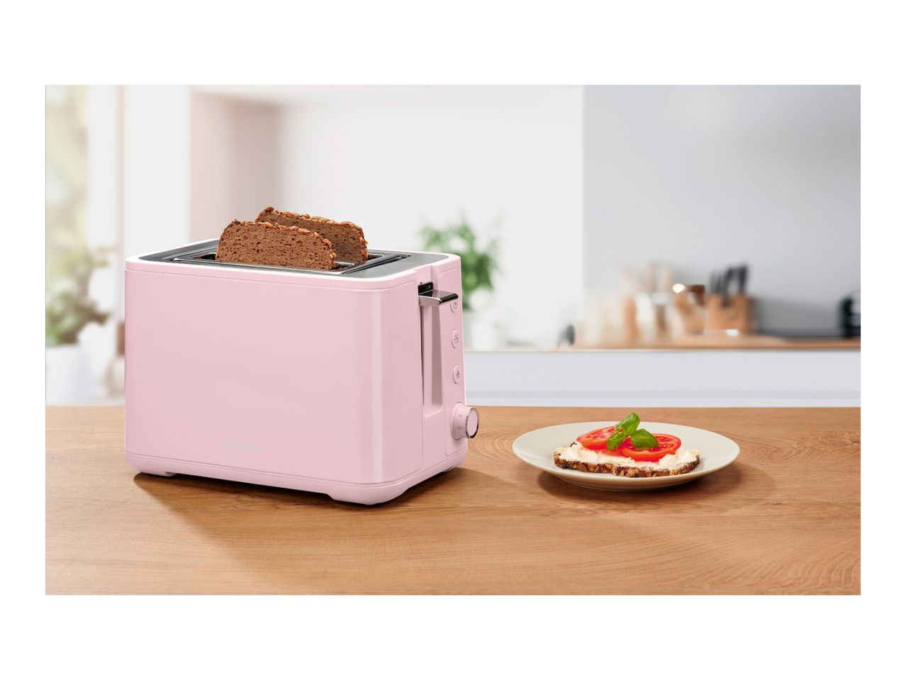 Pink toaster with two slices of bread, next to a plate with a tomato and cream cheese toast.