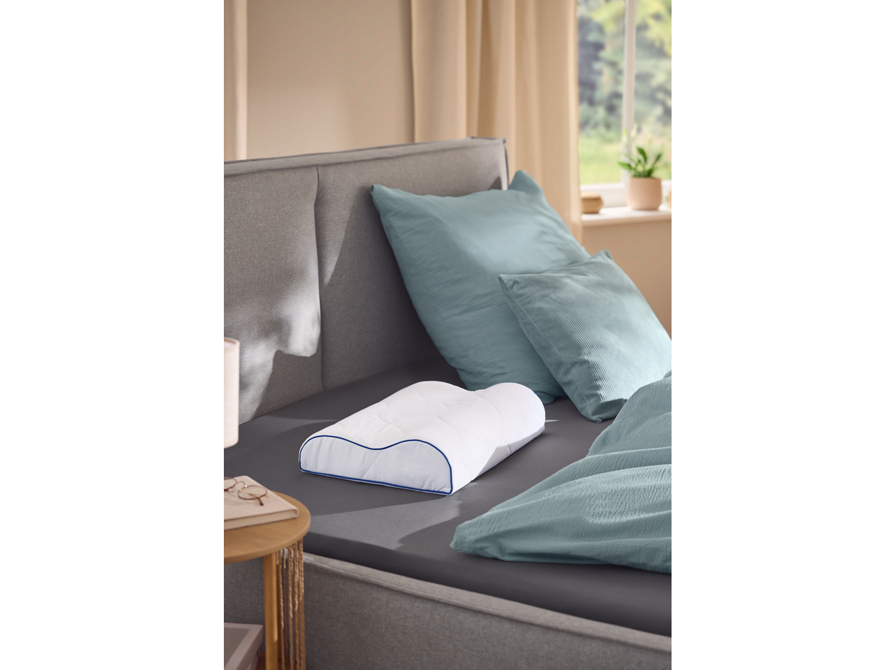 Livarno TopCool Neck Support Pillow on a bed with blue bedding and pillows.