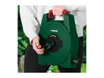Person holding a green hose reel with red handle and crank, ready for gardening.