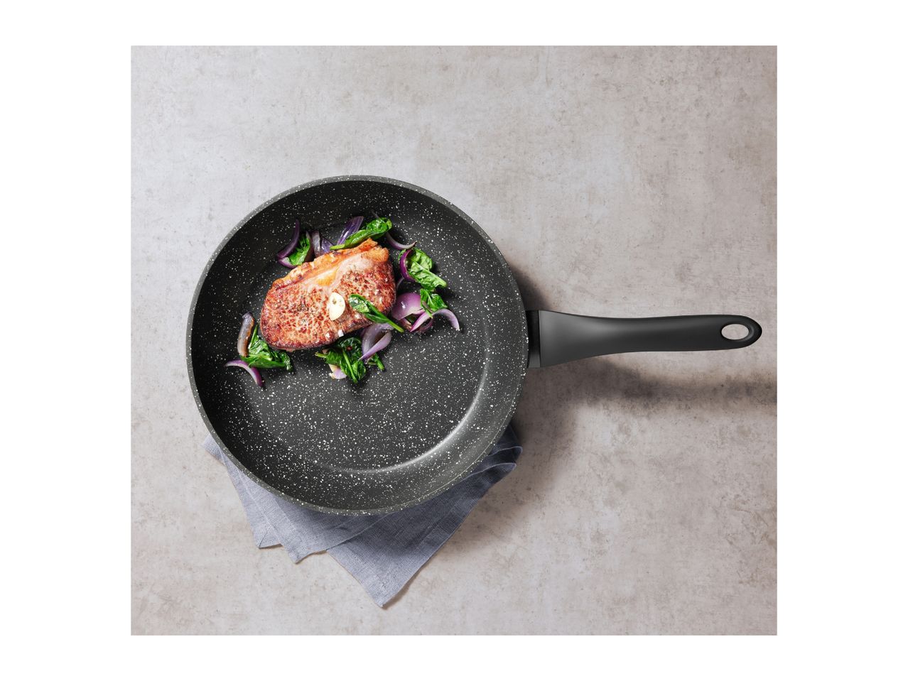 Frying pan with a cooked steak, red onions, and spinach on a grey surface.
